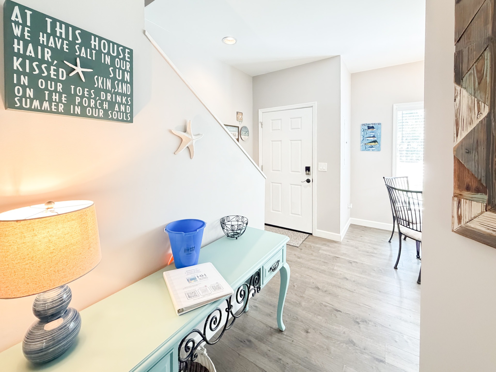 Coastal foyer with a mint-green console table, starfish wall decor, and a white front door under soft lighting.